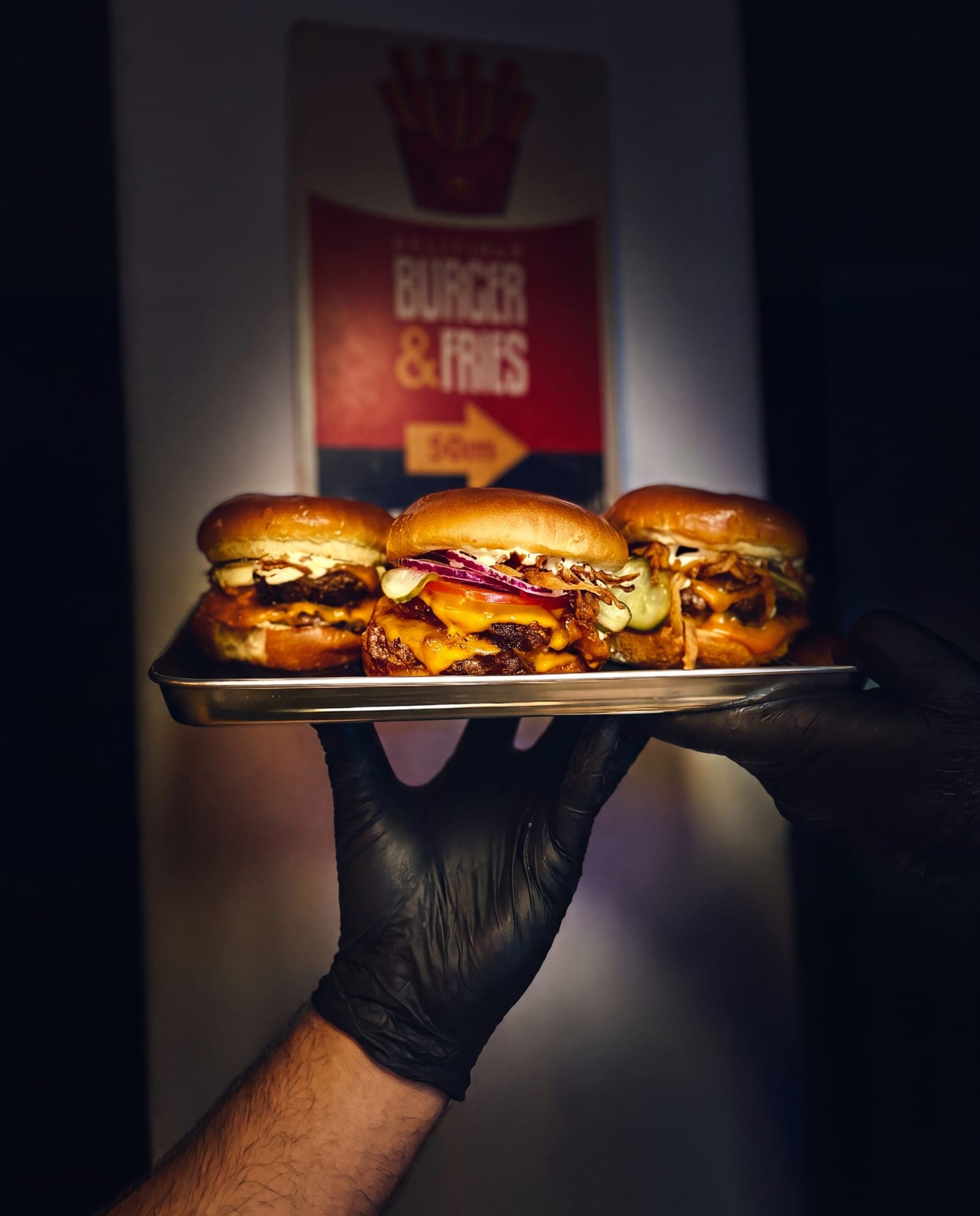 Drei Burger auf einem Metalltablett vor einem roten Burger-und-Fries-Schild